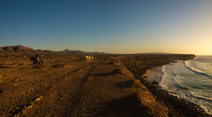 Beautiful sunset over the rocky coast of Fuerteventura,riders riding on a cliff