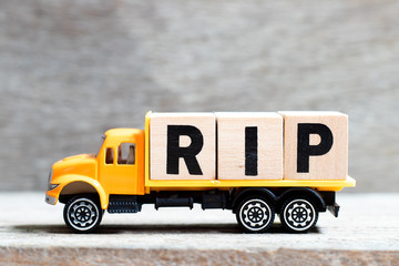Truck hold letter block in word RIP (abbreviation of rest in peace) on wood background