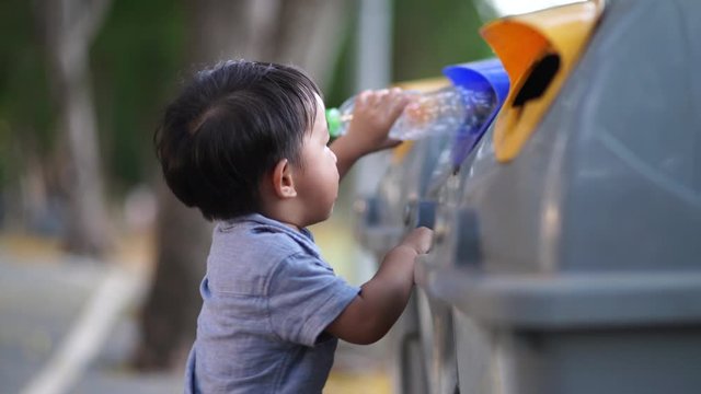 Adorable little boy keep clean plastic water bottle into trash bin in park ecologic world concept