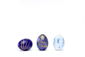 Three easter eggs trendy colored classic blue, white and golden decorated on white table. Happy Easter card with copy space for text. Minimal style.