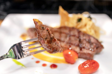 Medium grilled striploin beef steak with spaghetti olio a side dish served on white dish.
