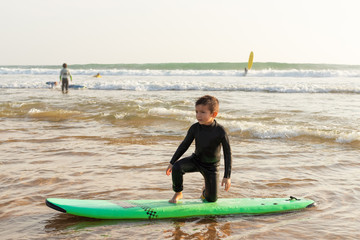 Little boy standing on surfboard. Adorable child in wetsuit standing on surfboard and looking aside...