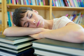 student sleeping on books in library