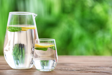 Glass and jug of fresh cold water on table outdoors