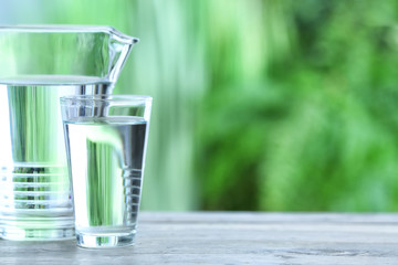 Glass and jug of fresh cold water on table outdoors