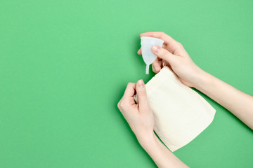 Female hands take menstrual cup from canvas bag. Zero waste composition on green background.