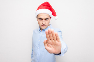 Serious guy in Santa Claus hat doing stop sign, portrait, white background
