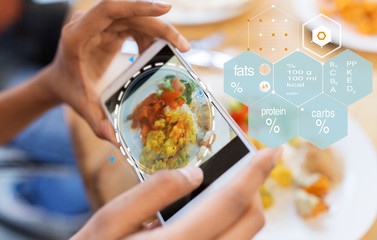 technology, eating and people concept - close up of hands with food on smartphone screen at restaurant over nutritional value chart
