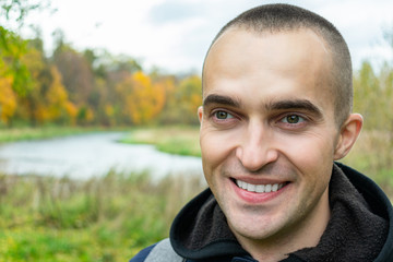 Joyful guy with a backpack smiles, man in the background of a beautiful landscape, close up, toned