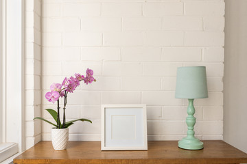 Closeup of purple moth orchid, blank square white picture frame and teal lamp on wooden table...
