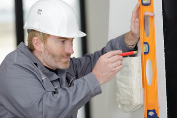 builder in helmet is measuring wall with level