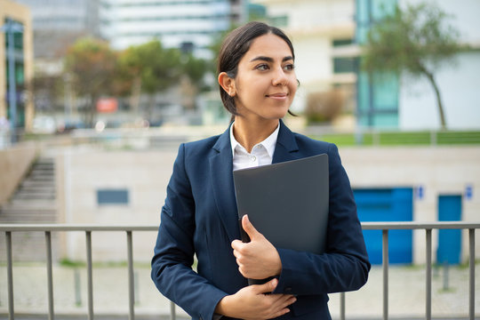 Happy businesswoman holding folder. Smiling young businesswoman in formal wear holding papers and looking aside on street. Professional occupation concept