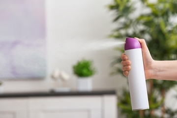 Woman spraying air freshener at home