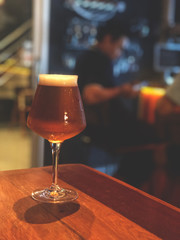 Defocused blur of scene inside of beer cafe. Glass of craft beer on the wooden table with dark cafe light.