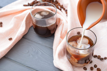 Pouring of milk into cold coffee in glass on table