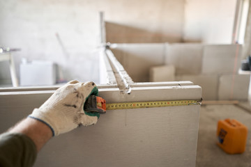 The construction worker measures with a tape measure Gypsum plate. Construction of internal walls...