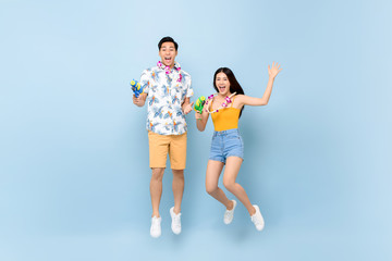 Young Asian couple in summer outfits with water guns jumping in studio blue background for Songkran festival in Thailand and southeast Asia