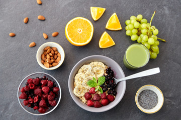 food and breakfast concept - oatmeal cereals in bowl with wild berries, fruits and glass of juice on slate stone table