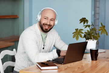 An adult attractive man with headphones is working at the computer in the kitchen. A stylish person enjoys success in business. Work online. Business portrait