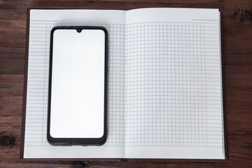 The phone with the screen on lies on an open notebook in a cage on a wooden table.