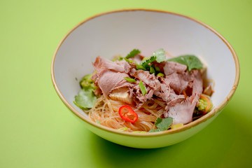 Rice noodles with beef and vegetables served in a white bowl over bright green background.