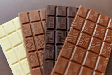 sweets, confectionery and food concept - milk, dark and white chocolate bars on brown background