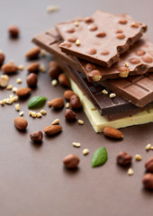 sweets, confectionery and food concept - bars of dark, white and milk chocolate with nuts on brown background