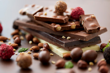 sweets, confectionery and food concept - close up of different chocolate bars, candies and nuts on brown background
