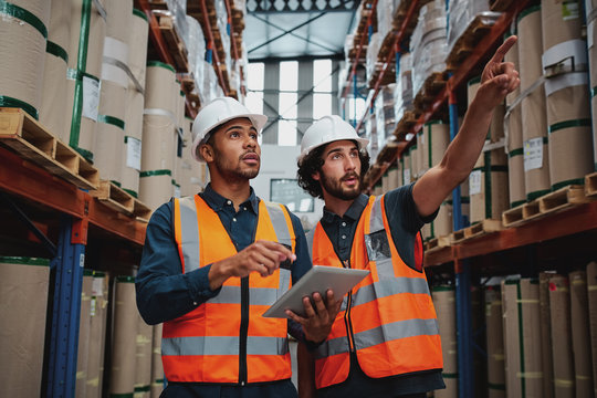 Tensed Worker In Factory Showing Shelves To His Manager Holding Digital Tablet With Hardhat And Safety Vest