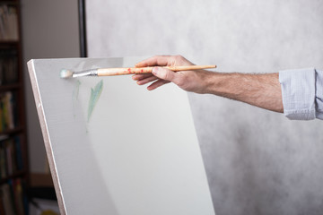 Artist's hand with a brush paints on a white canvas. The beginning of a picturesque picture