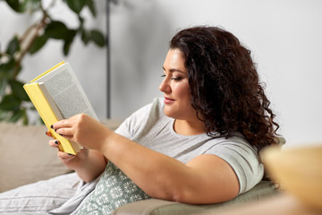 people and leisure concept - young woman reading book on sofa at home