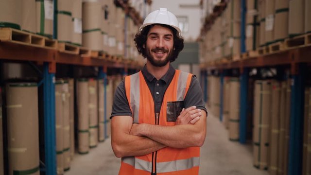 Confident smiling young warehouse entrepreneur looking at camera with his arms crossed