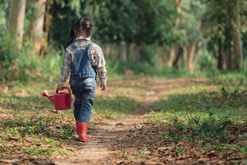Asian little girl holding red watering tree walking in nature. First learning of little children. Happy family concept. Rear view shot