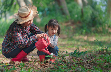Asian little girl with mom planting and watering tree in nature. First learning of little children.