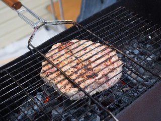 A large piece of meat is cooked on a charcoal grill. Cooking outdoors
