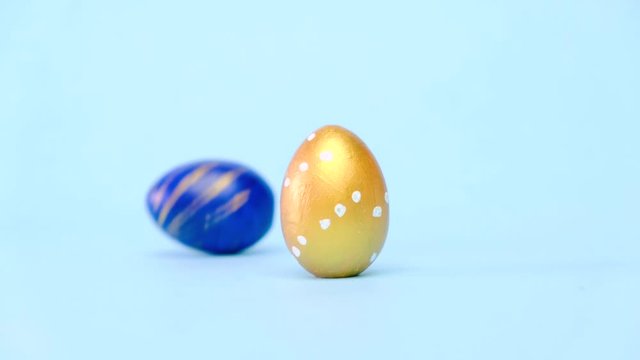 Easter eggs are rolling, knocking each other on blue table. Eggs trendy colored classic blue, white and golden . Happy Easter. Minimal style