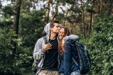 Young couple with backpacks on their backs smiling and walking in the forest, enjoy the walk