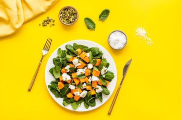 Light dish for lunch. Salad with pumpkin and basil on yellow background top-down