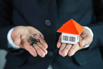 Real estate agent holding house model and keys,  customer signing contract to buy house, insurance...