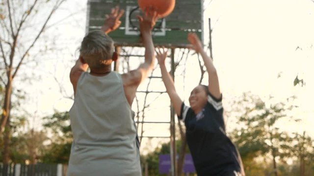 Asian senior father playing basketball with his daughter on stadium on summer day. Happy family spending free time together. Healthy lifestyle concept.