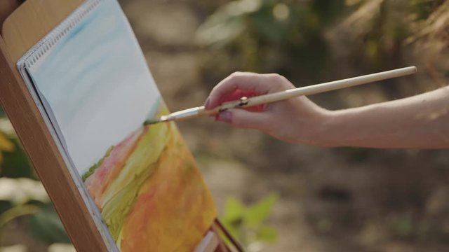 Female hand painting a landscape with watercolors on sunny nature