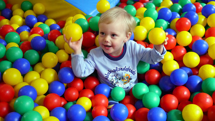 Fototapeta na wymiar Dziecko wśród kolorowych kulek na placu zabaw w bawialni, chłopiec bawi się kulkami, dziecięce zabawy wśród plastikowych kulek. Trzyma w rękach dwie kulki.