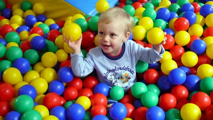 Fotobehang Dziecko wśród kolorowych kulek na placu zabaw w bawialni, chłopiec bawi się kulkami, dziecięce zabawy wśród plastikowych kulek. Trzyma w rękach dwie kulki. © Marcin
