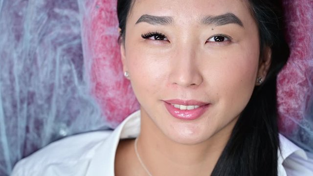 Portrait of a beautiful asian woman opens her eyes during eyelash extension procedure. Double eyelash volume before and after.