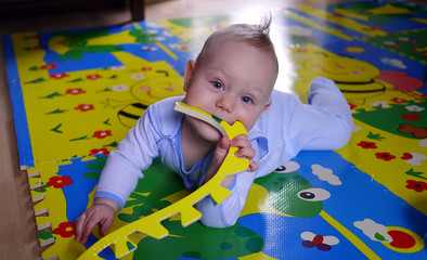 Chłopiec gryzie kawałek maty do raczkowania. Małe dziecko bierze wszystko do buzi. Mata jak gryzak. Raczkujący chłopiec, uśmiechnięty i zadowolony, psoci i dokazuje. © Marcin