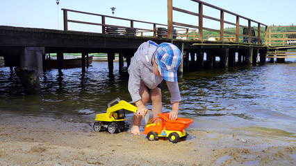 Dziecko bawi się na plaży obok molo. Chłopiec bawi się samochodami budowlanymi - koparka i wywrotka. © Marcin