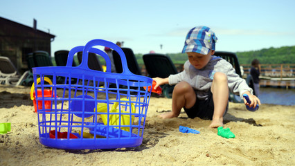 Dziecko na plaży bawi się w piasku. Wakacyjna zabawa nad woda na plaży.  Urlop nad jeziorem. - obrazy, fototapety, plakaty