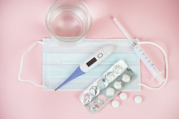 Medical masks, medications, pills, pills, thermometer and syringe for the coronavirus epidemic. A set of medicines for the treatment of coronavirus lies on a pastel background. Top view