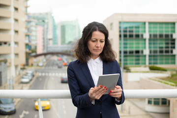 Focused woman using tablet pc. Serious middle aged businesswoman using digital tablet while standing on urban city street. Wireless technology concept