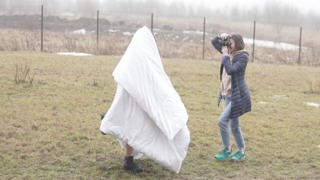 A female photographer is photographing a model in a blanket outside. Creative photo for dating site